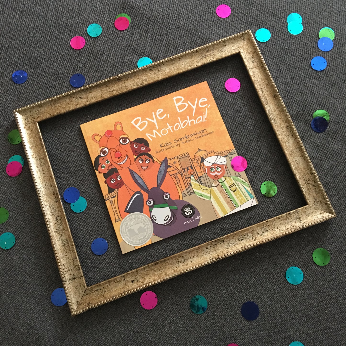 Book in a gold photo frame surrounded by colorful dots